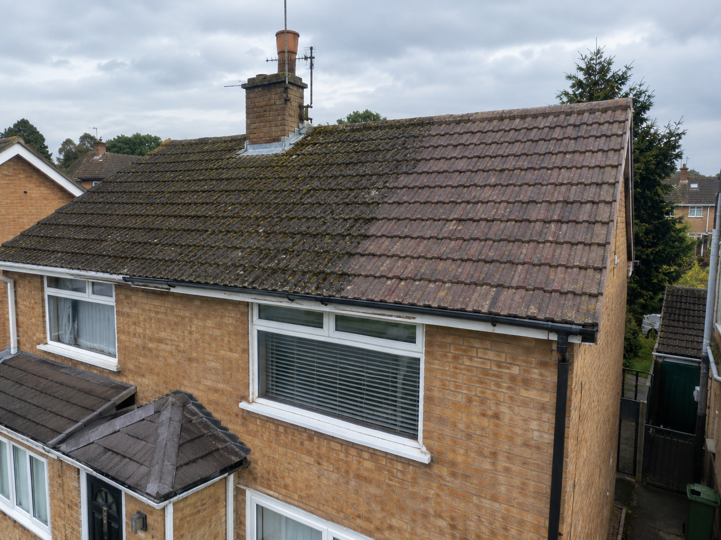 Tile roof with moss removed on one half and still dirty on the other
